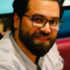 A man with dark hair and a beard, wearing glasses and a light blue shirt, sits indoors and smiles at the camera, reflecting the friendly professionalism often found in Bookkeeping and Accounting Services.
